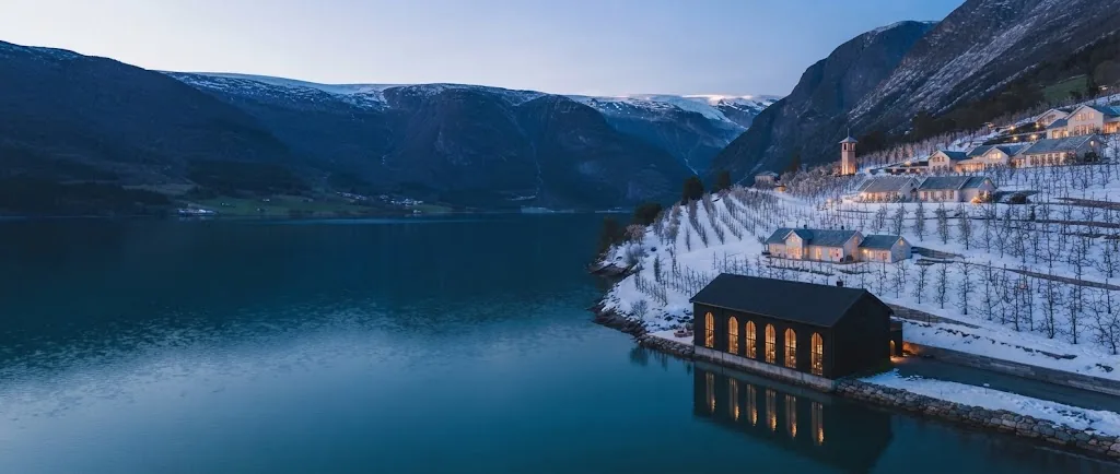 Artist's impression of the fjord at blue hour, with the resort's warm windows among the orchards on the right