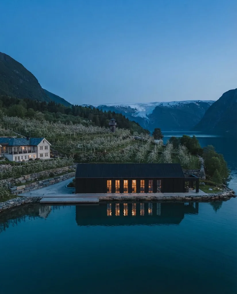 Artist's impression of Kvasir's Hall in the evening, a long dark-timber hall with warm windows over the water